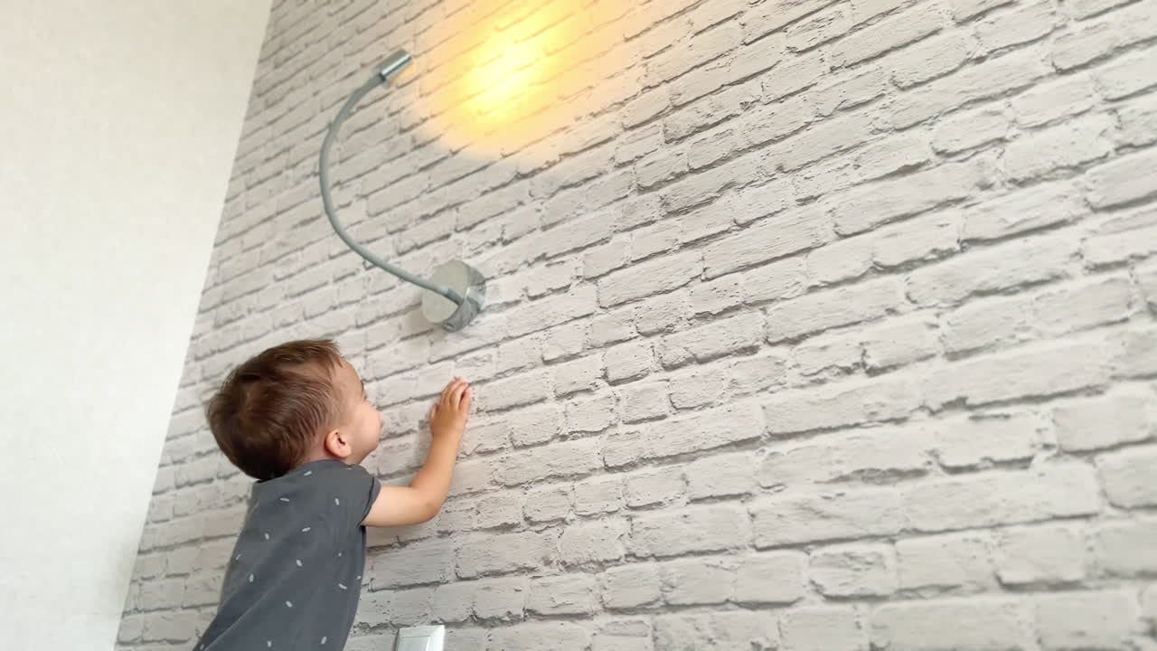 Happy toddler switching on the light on the wall. Adorable kid is smiling playing with the lamp. Low angle view.