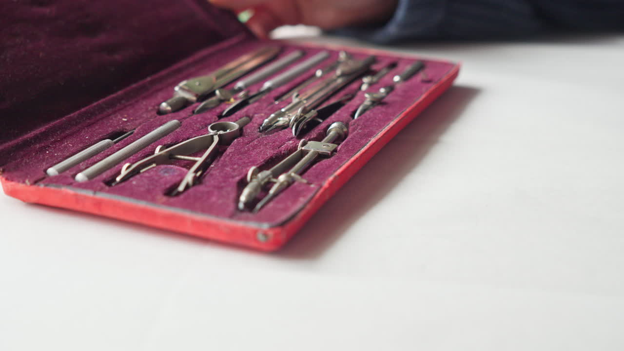 Hands open a compartmented case to reveal a full drafting set, suggesting readiness, expertise, and professional design practice