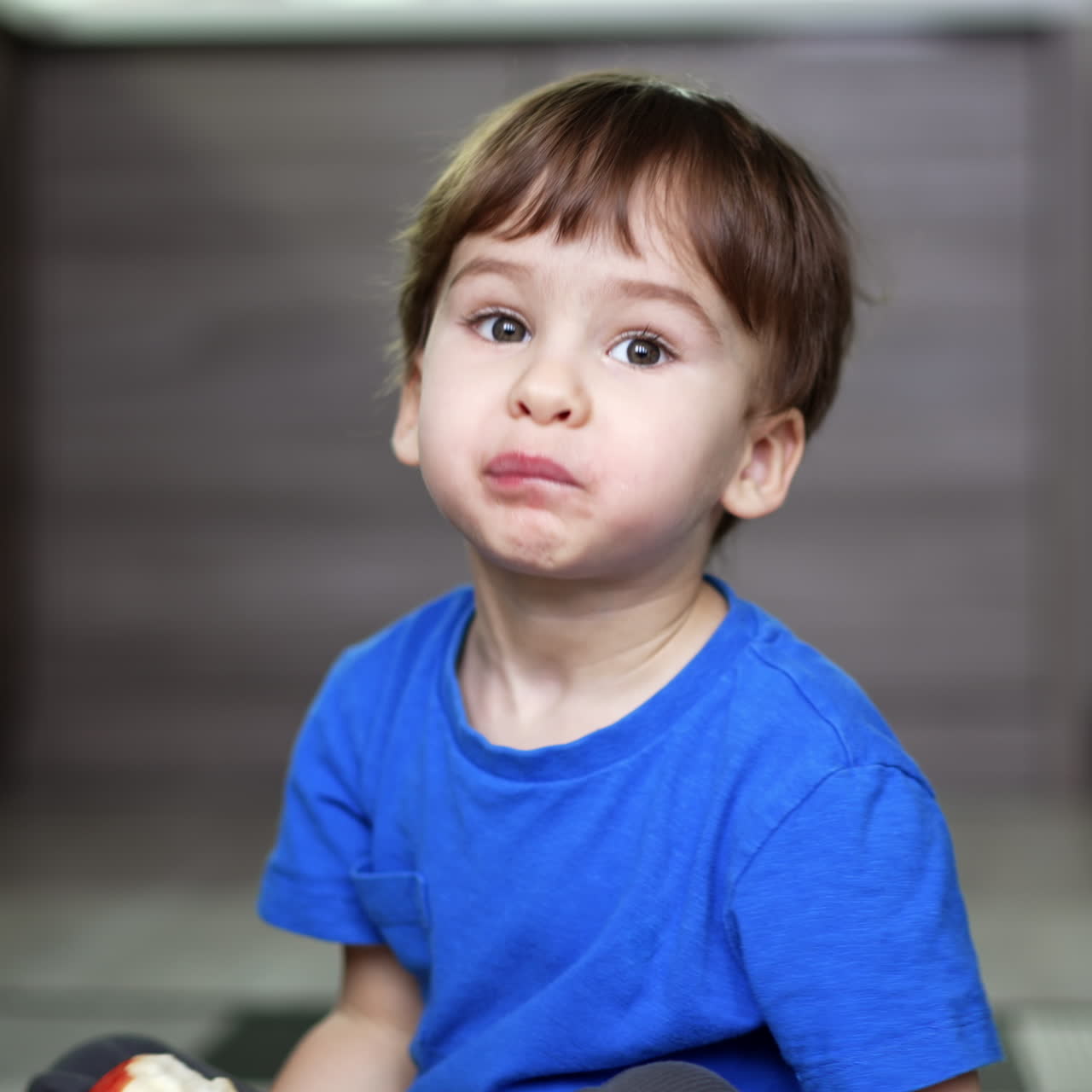 Niño pequeño de dos años con cabello oscuro comiendo una manzana. El niño mueve la cabeza juguetonamente mientras come.