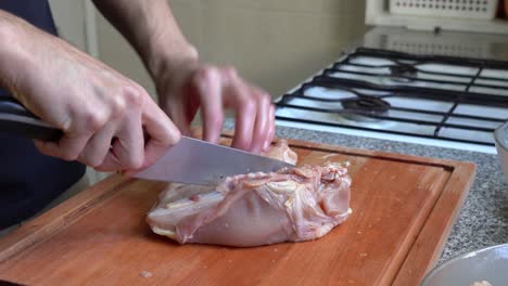 A-Person-Cutting-Whole-Breast-Chicken-In-Two-Wooden-Board-At-Home-Kitchen