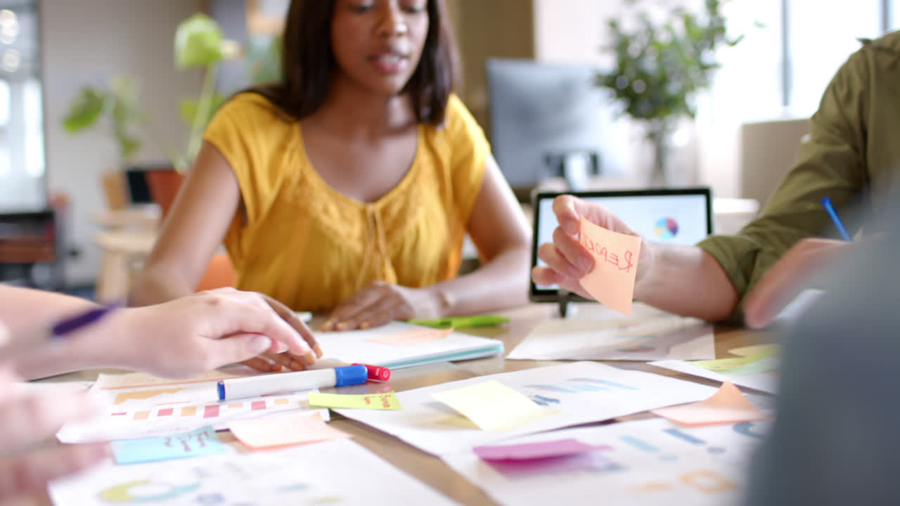 Happy diverse colleagues brainstorming with documents and tablet at table in office in slow motion