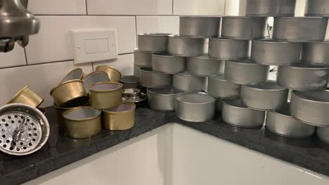 panning-right-to-left,-inside-home-near-kitchen-sink,-shot-of-stacked-proofing-pans-and-opened-cans-and-lids,-close-up