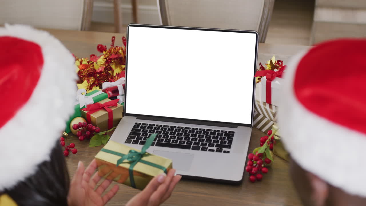 animación de una pareja diversa con sombreros de santa usando una computadora portátil con pantalla en blanco en navidad