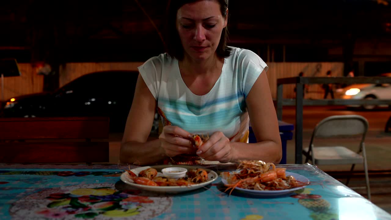 comida callejera. una mujer está mojando un camarón en una salsa y comiendo.
