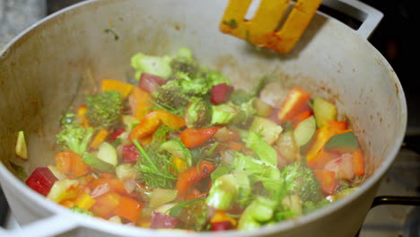 wooden spatula stirring vegetable pot with broccoli, beetroot, carrots with steam rising from it