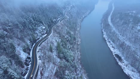 Luftaufnahmen-Einer-Verschneiten,-Malerischen-Nebenstraße,-Einer-Kurvenreichen-Bergtalstraße-Während-Eines-Schneesturms-Mit-Kiefern,-Einem-Fluss,-Einer-Bergstraße,-Felsigen-Klippen-Und-Wäldern-Im-Winter-An-Einem-Kalten,-Blauen-Tag