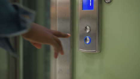 close-up shot of hand pressing elevator button with illuminated blue arrow pointing upwards on control panel. modern elevator with metallic design and green walls, indicating movement to upper floor