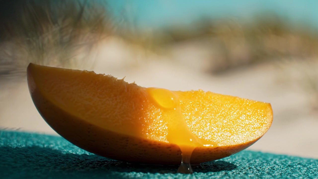 Vivace fetta di mango succoso che mostra la sua polpa arancione brillante con nettare che cola su una superficie morbida sotto luce naturale e uno sfondo sfocato.