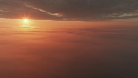 Slow aerial pan of sun shining above thick cloud cover during brilliant sunrise.