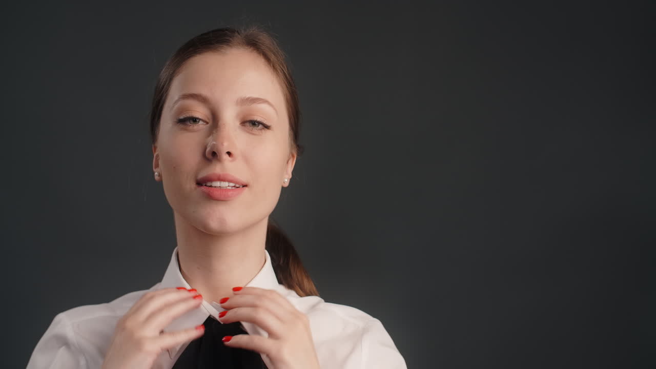 Woman adjusting hair in a formal white shirt and black tie