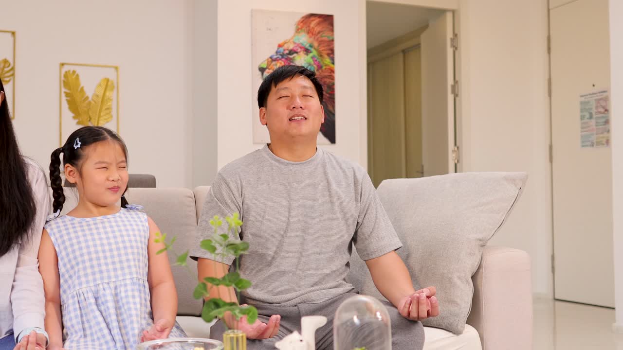 A family meditates together on a sofa in a bright, cozy living room, fostering calm and connection