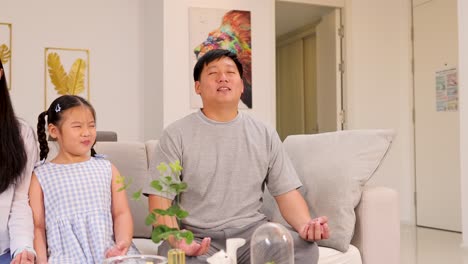 a family meditates together on a sofa in a bright, cozy living room, fostering calm and connection