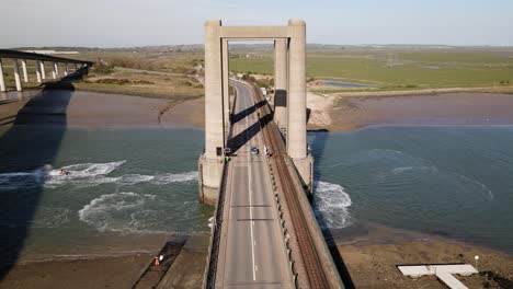 Aerial-View-Of-The-Railway-And-Road-At-The-Kingsferry-Bridge-With-A-Vast-Meadow-On-The-Backdrop-In-England