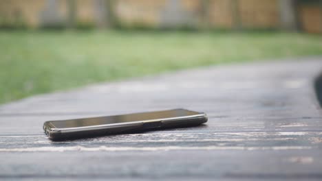 a black smartphone lying on a wooden bench in a park.