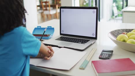 feliz muchacho biracial sentado en la mesa usando una computadora portátil con espacio de copia y teniendo clases en línea