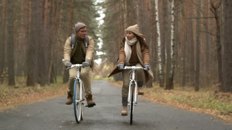 Front-View-Of-A-Couple-Wearing-Winter-Clothes-Riding-Bikes-In-The-Forest-While-Raining-1