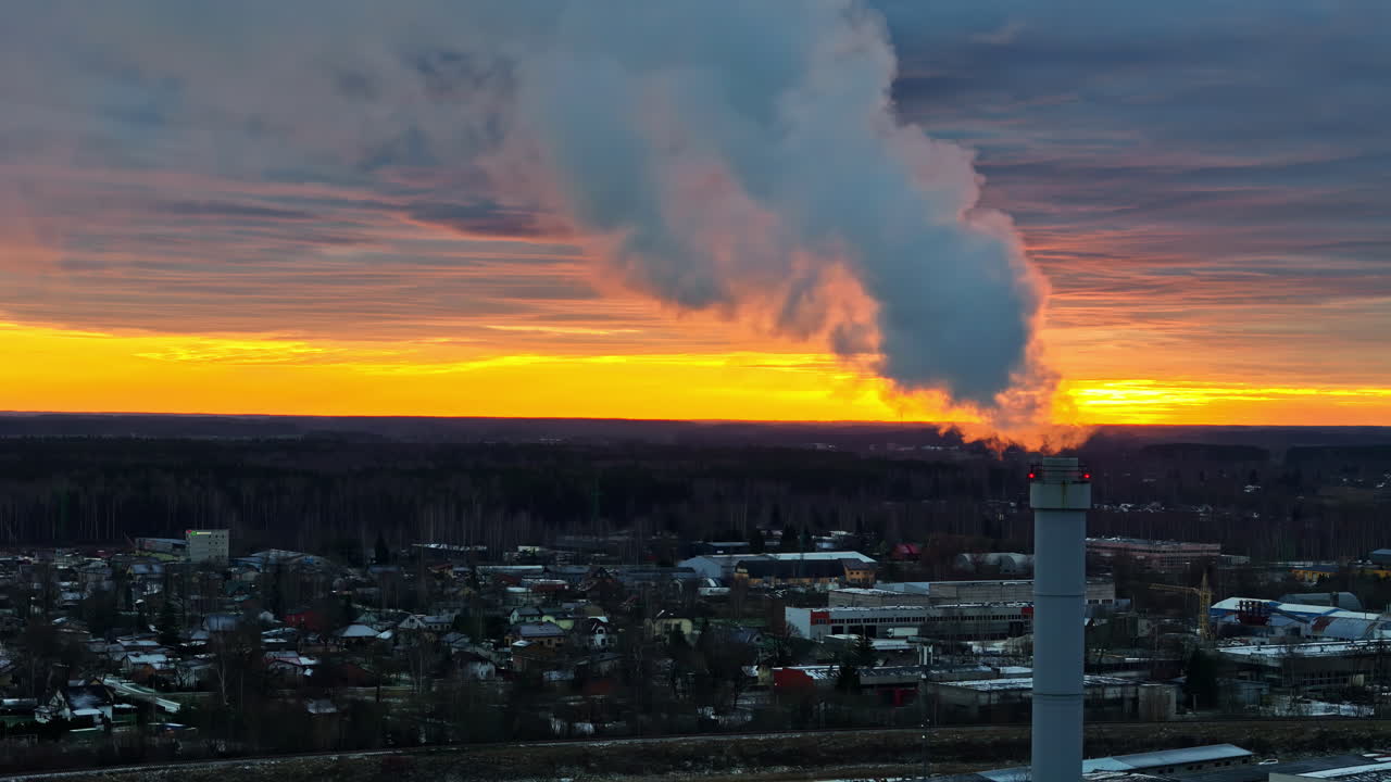 Industrial chimney emits smoke against vibrant sunset sky