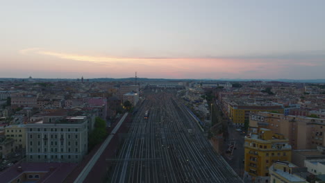 Aerial-slide-and-pan-footage-of-wide-railway-body-with-multiple-tracks-leading-through-city.-Roma-Termini-train-station-at-dusk.-Rome,-Italy