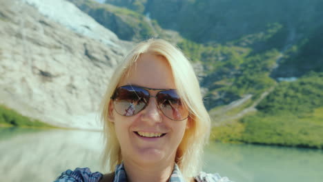 a woman in sunglasses shoots herself on video against the backdrop of the mountains and the glacier