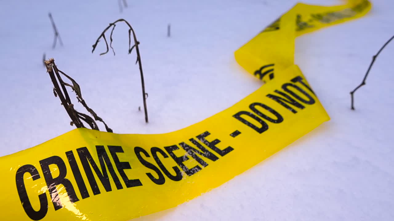 Wrinkled crime scene tape lying on fresh snow with light snowfall and blurred winter background, creating a dramatic forensic mood