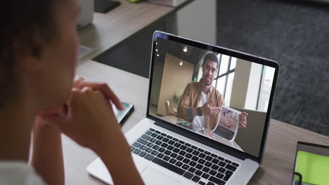 sección media de una mujer afroamericana haciendo una videollamada en una computadora portátil con un colega masculino en la oficina