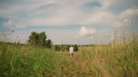 lady walks through grassy field on sunny day holding dangling rope in her hand, surrounded by wide open landscape with trees in distance under blue sky