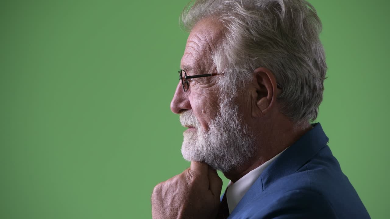 Handsome senior bearded businessman against green background