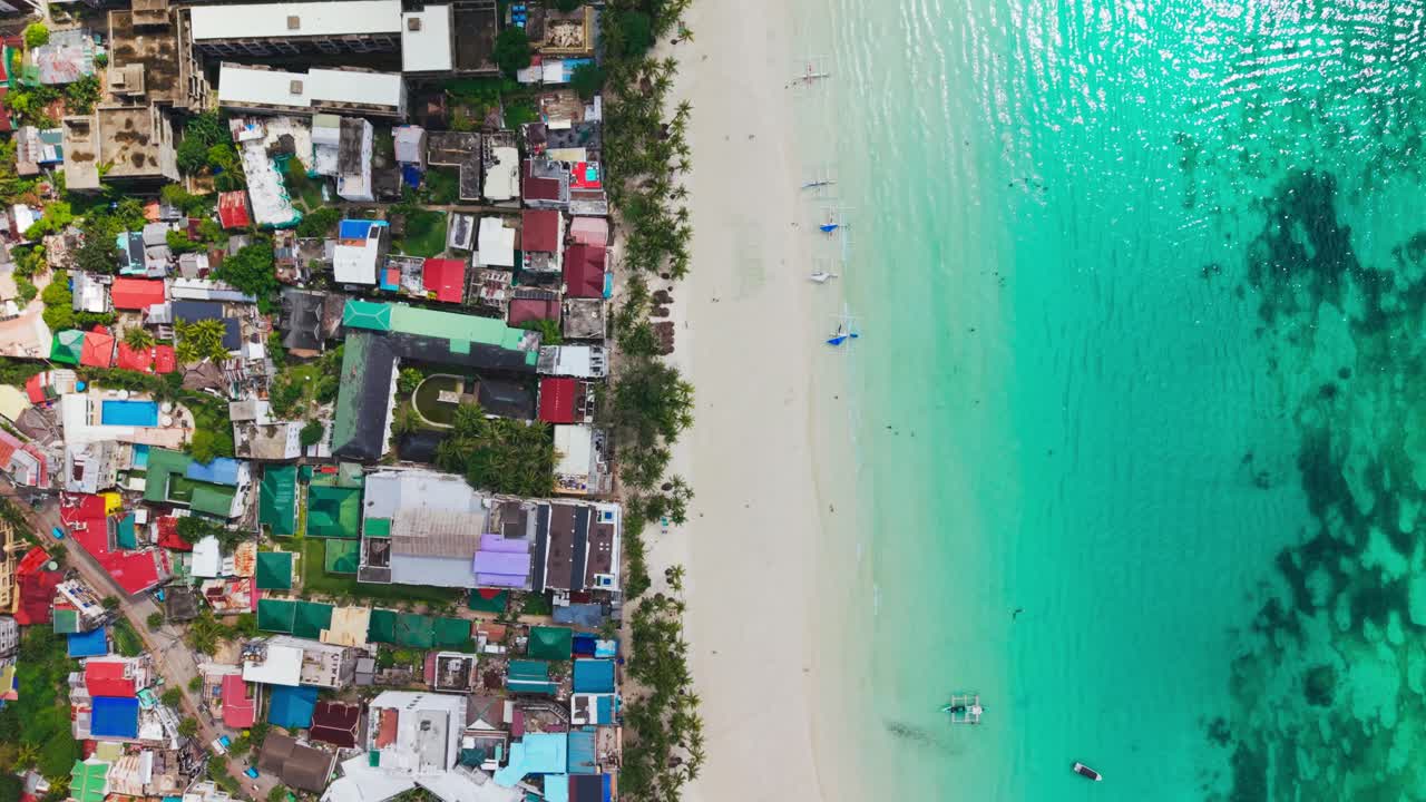 Un lento movimento all'indietro con drone rivela i tetti di un resort, una spiaggia sabbiosa e un mare poco profondo color acqua