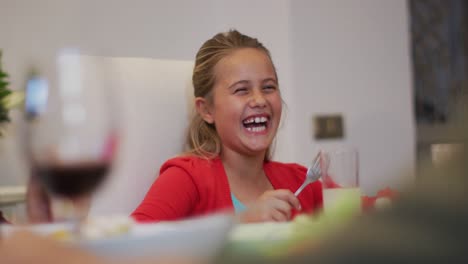 Happy-caucasian-sister-laughing-watching-brother-eating-at-table-during-family-meal