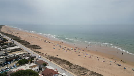 Panning-high-up-over-orange-beach-and-sea-revealing-small-fishing-town-during-the-day