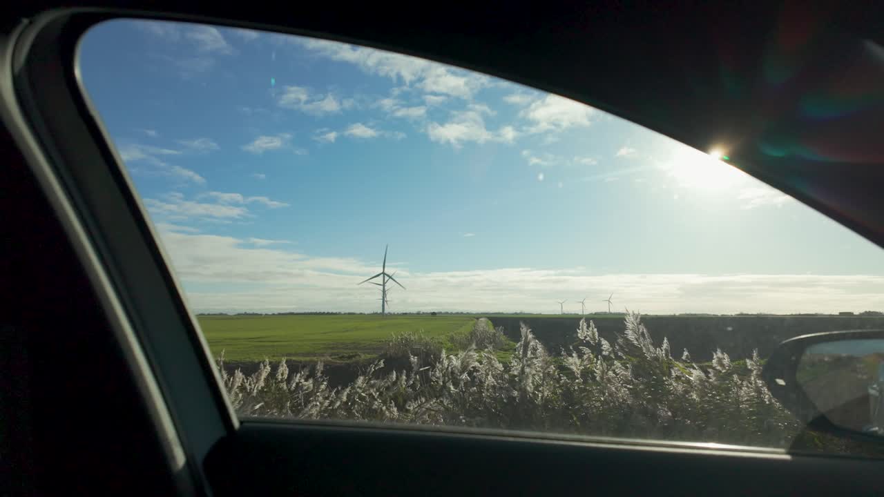 Static shot of fields and wind turbines through a car window