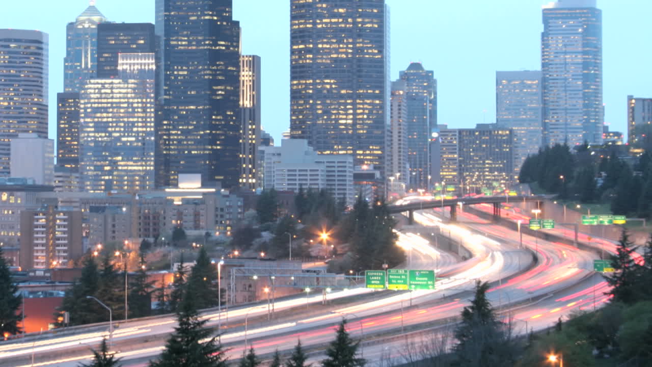 a medida que la hora dorada se oscurece en la noche, el tráfico acelerado se desdibuja en rayos de luz ante un horizonte de seattle iluminado