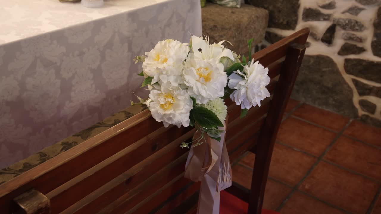 elegant white flower bouquet tied with ribbon decorates wooden pew for wedding ceremony
