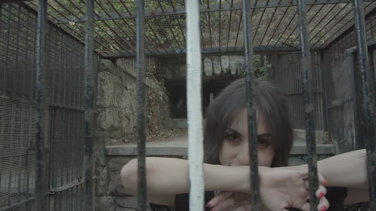 금속 격자에 갇혀 버려진 동물 우리에서 어두운 옷을 입은 여자