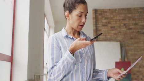 Video-of-happy-biracial-female-designer-using-smartphone-in-studio