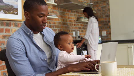 Padre-E-Hija-Usan-Una-Computadora-Portátil-Mientras-La-Madre-Prepara-La-Comida