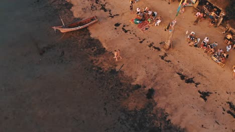 Vuelo-Aéreo-De-Regreso-Contra-Personas-Sentadas-En-El-Bar-De-La-Playa-En-Una-Isla-Tropical-Durante-La-Puesta-De-Sol