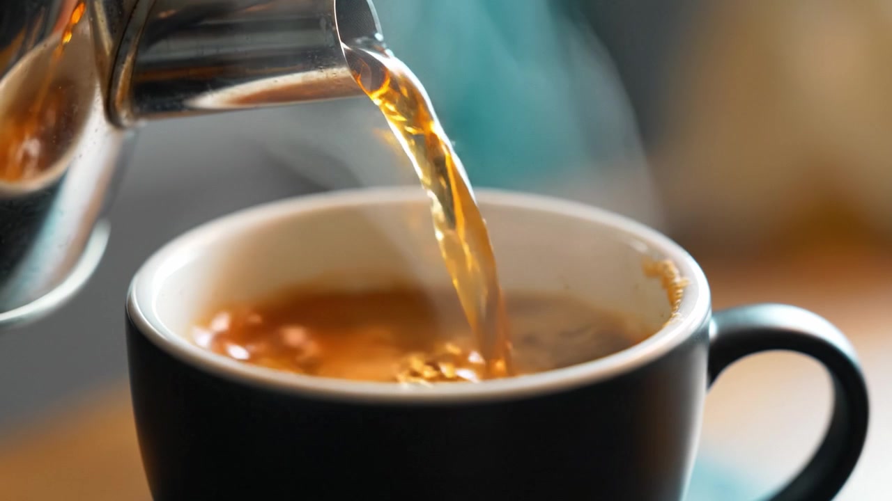 Versare caffè appena fatto in una tazza nera con vapore che sale, catturando il momento dei rituali mattutini e degli aromi confortanti in un ambiente accogliente.