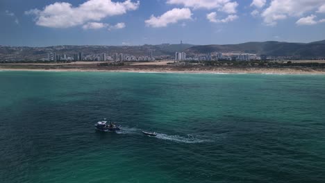 無人機圍繞著漁船, 投<unk>網, 顯示霍夫哈卡梅爾鎮在背景, 海法海灘和輝<unk>的天空