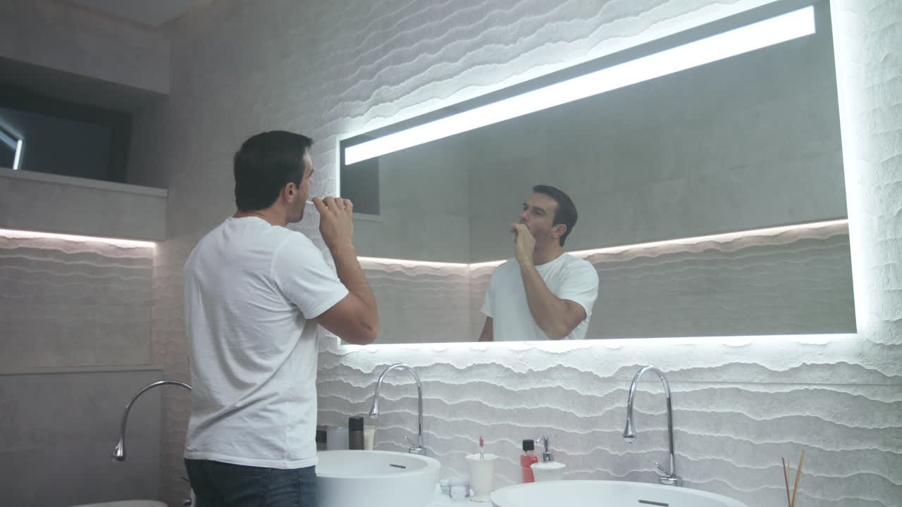 Uomo felice che si lava i denti in bagno. Un uomo concentrato si prende cura dei suoi denti.
