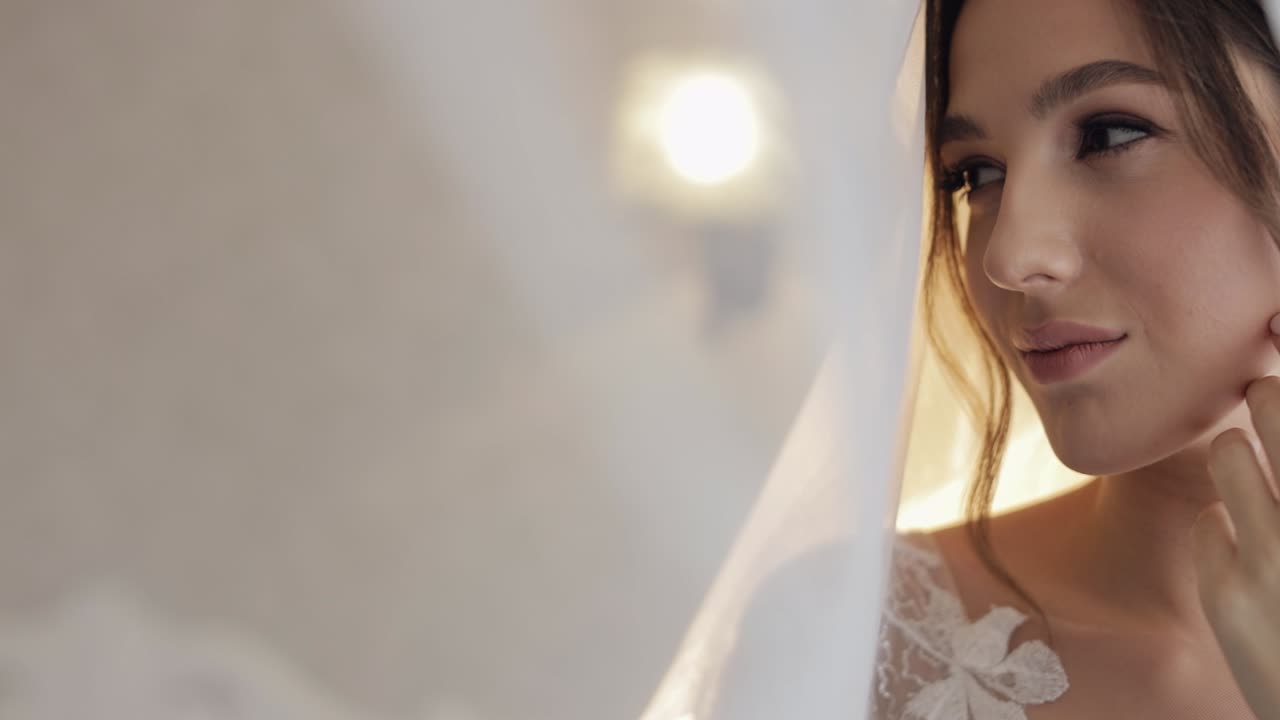 Noiva em vestido boudoir sob o véu e com um robe de seda. Preparativos matinais do casamento antes da cerimônia