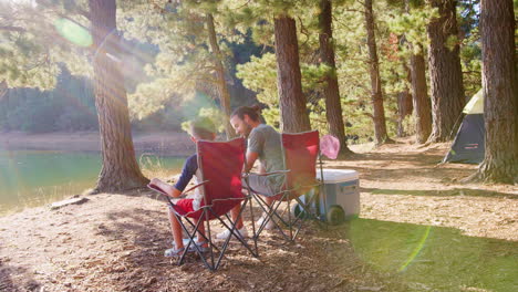 father and son sitting in camping chairs by lake skimming stones