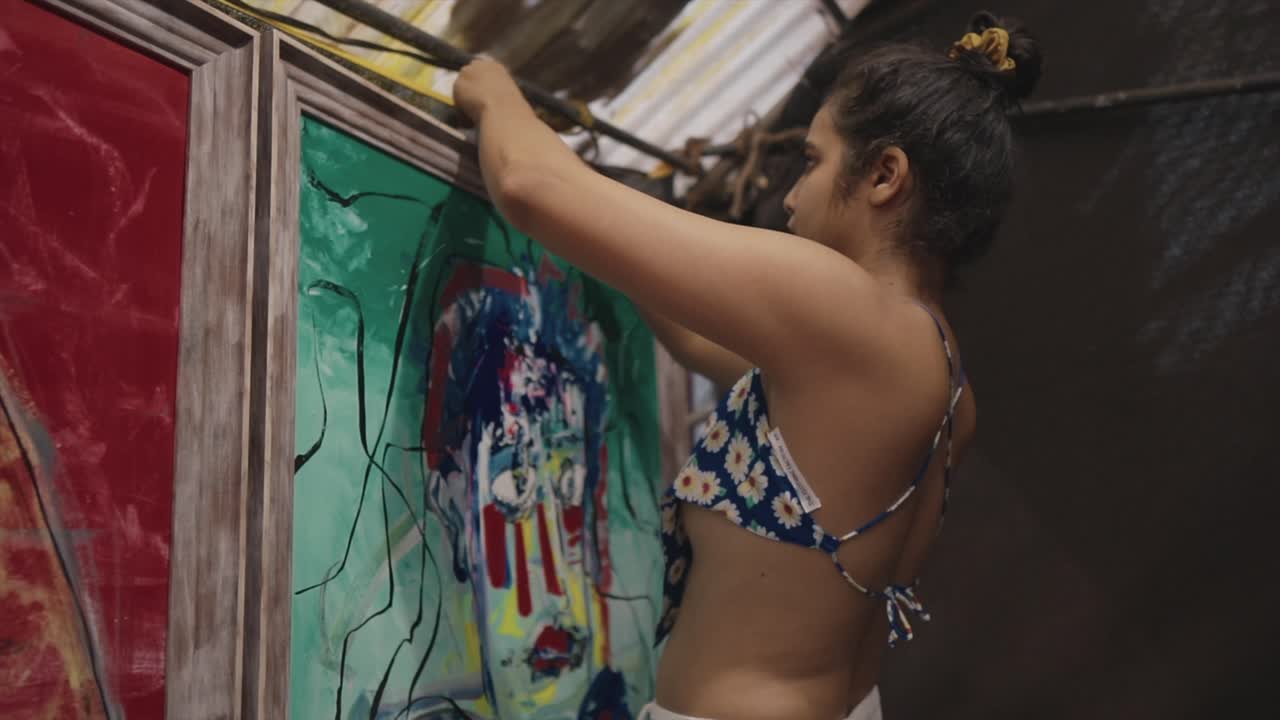 Menina pendurando pinturas em aquarela em molduras na parede de uma galeria de arte