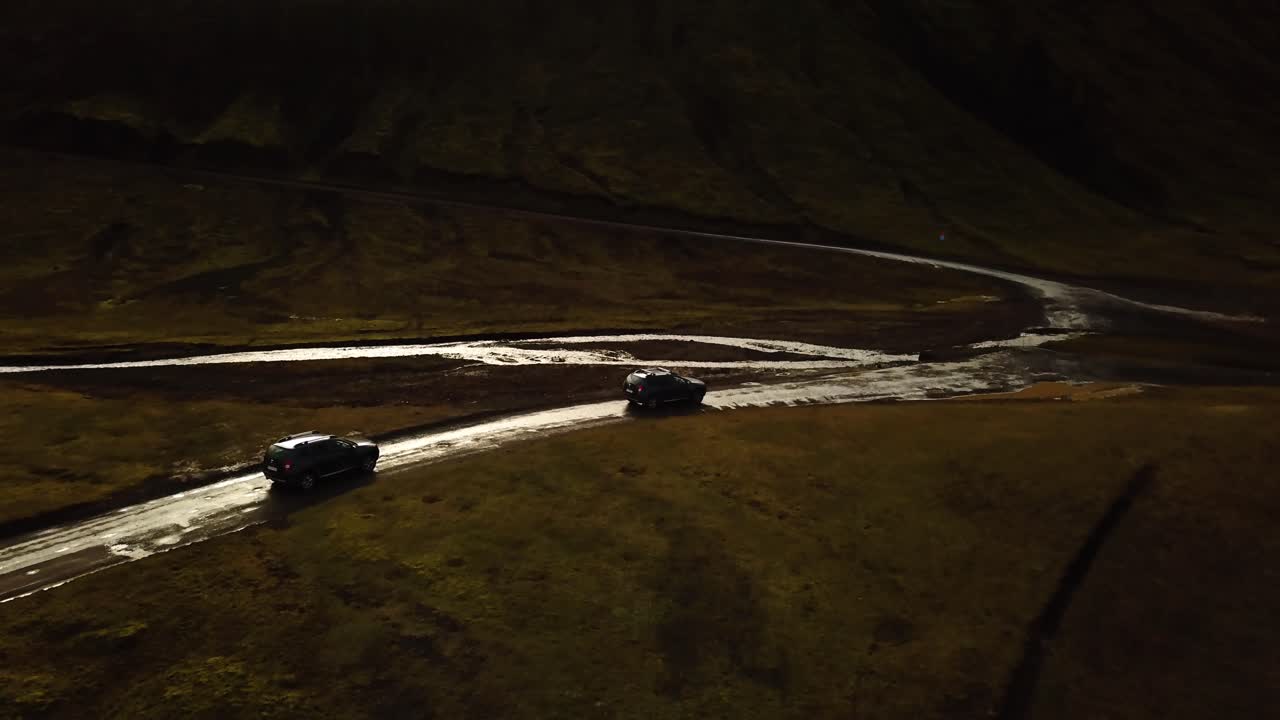 vista aérea del paisaje sobre los coches de tracción en las cuatro ruedas que viajan por un camino de tierra y cruzan un río fangoso, en las tierras altas islandesas