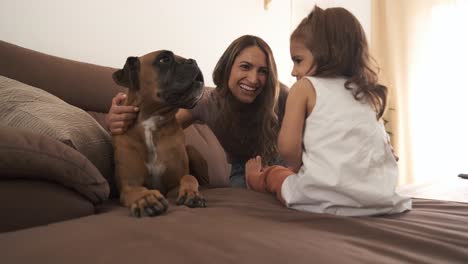 smiling mother helping daughter to touch pet dog on sofa