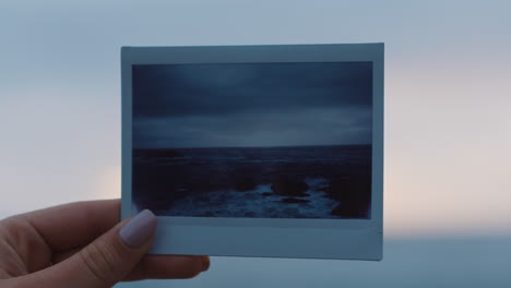 close up hand holding photograph of beautiful seaside ocean