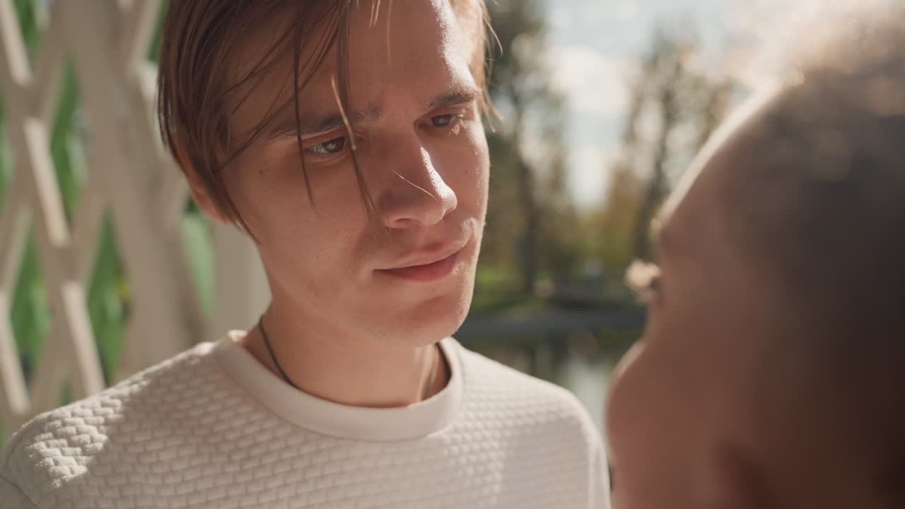White man gazing at black woman lakeside with soft sunlight through autumn trees, closeup on thoughtful expression and subtle tear, calm voice and quiet promise of commitment, contemplative mood