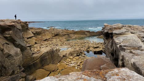 Male-Tourist-standing-on-cliff-watching-the-Atlantic-Ocean-on-the-Island-Île-Grande-in-Pleumeur-Bodou,-France-Cote-D'amour