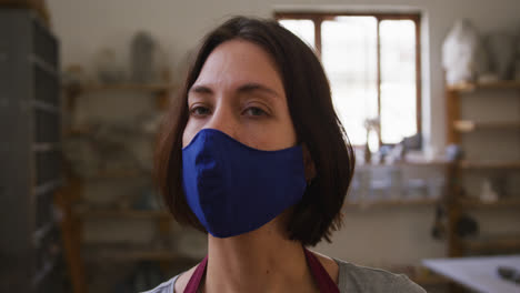 portrait of female potter wearing face mask and apron at pottery studio