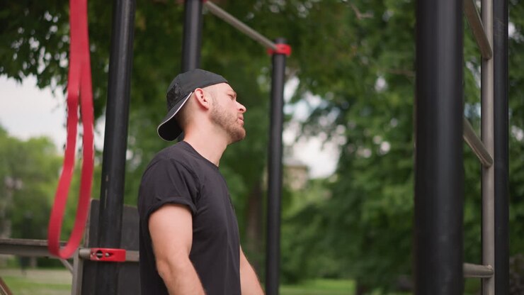Relaxed Outdoor Recovery, Man Stretches In Park Environment, Person Using Strap To Loosen Shoulder Muscles Outdoors, Male Figure In Park Engaged In Postsetup Muscle Relaxation Exercises